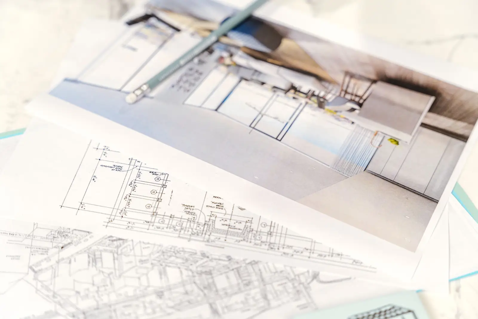 Architectural drawings and a rendering laid out on a desk with a pencil