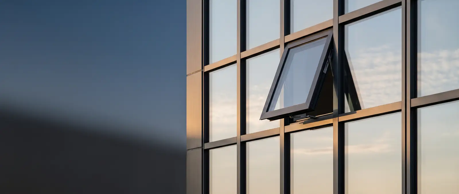 A single awning window open on a glass curtain wall facade at dusk